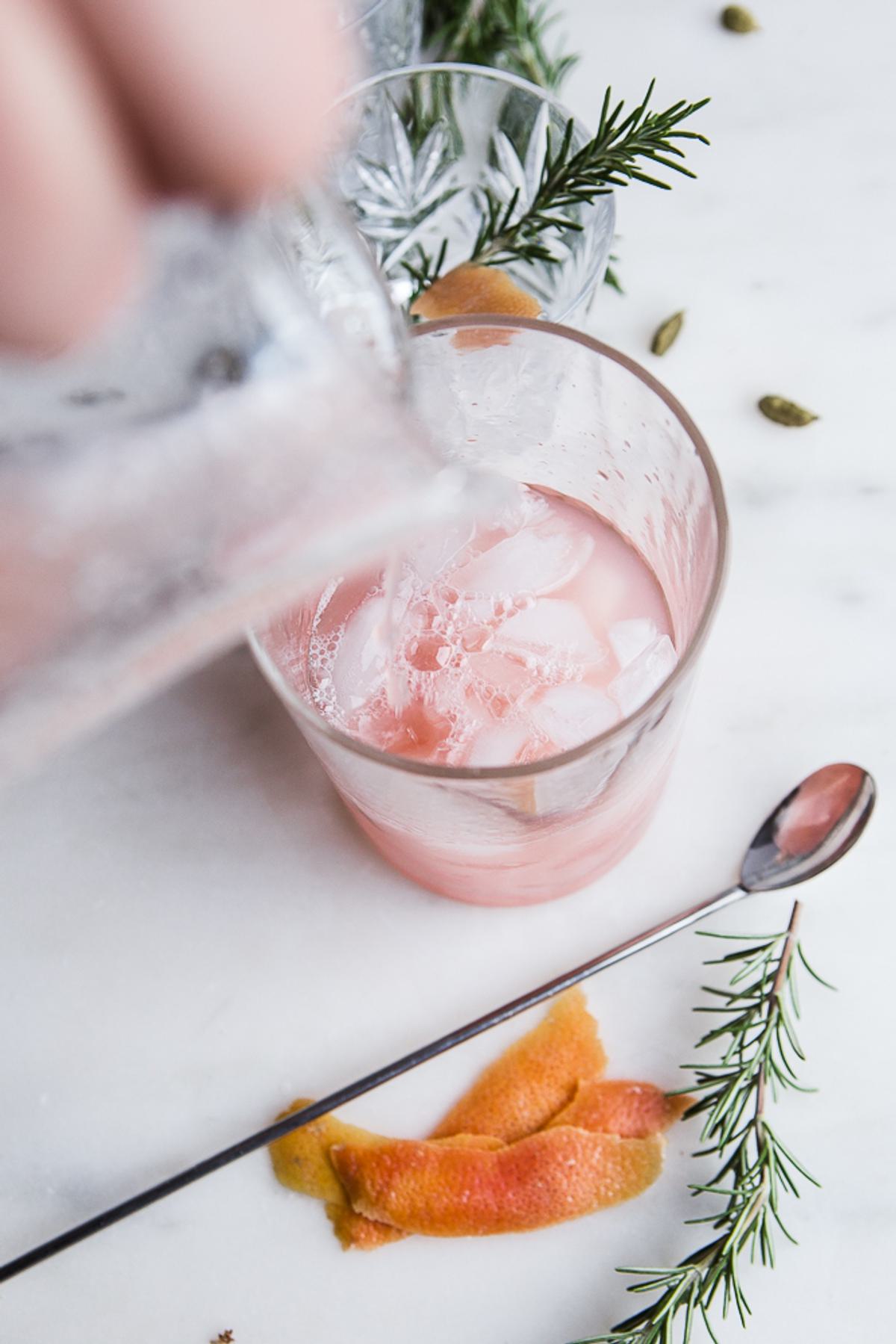 rosemary simple syrup being poured into Grapefruit Cardamom Gin Fizz