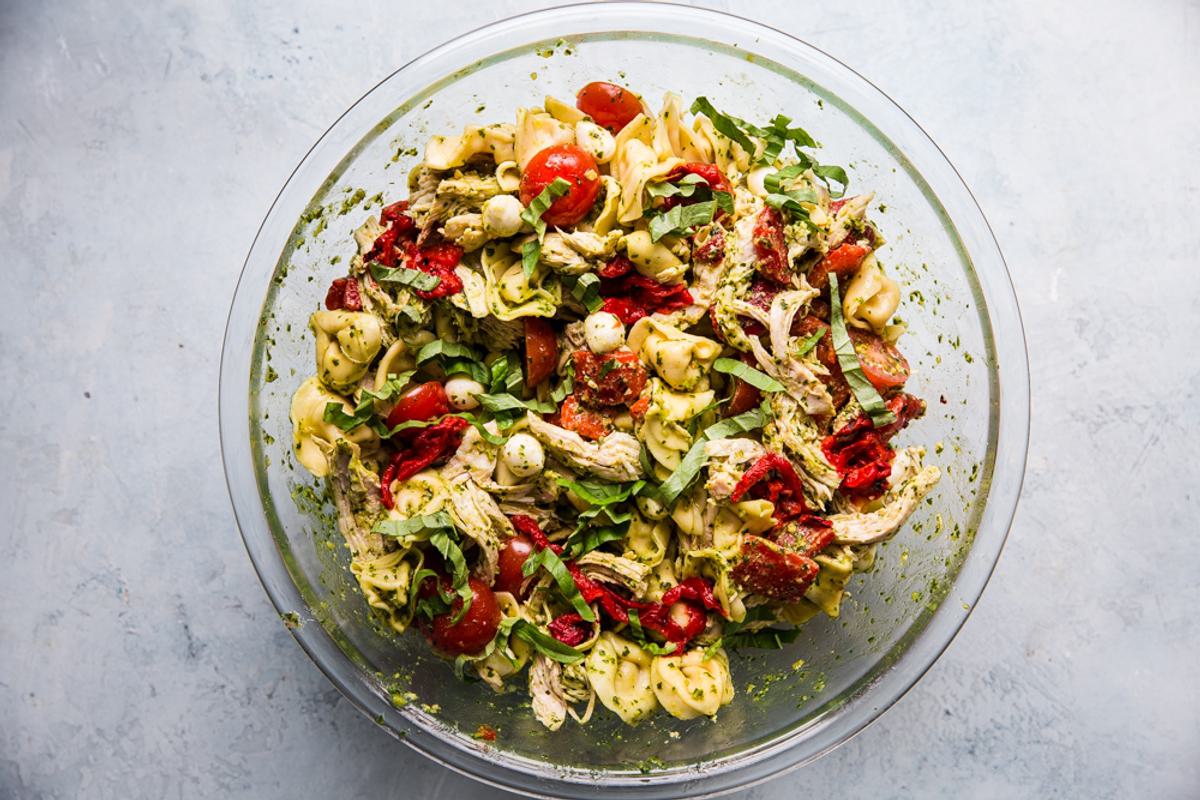 a large mixing bowl with tortellini, pesto, mozzarella, roasted red bell peppers, cherry tomatoes and shredded chicken