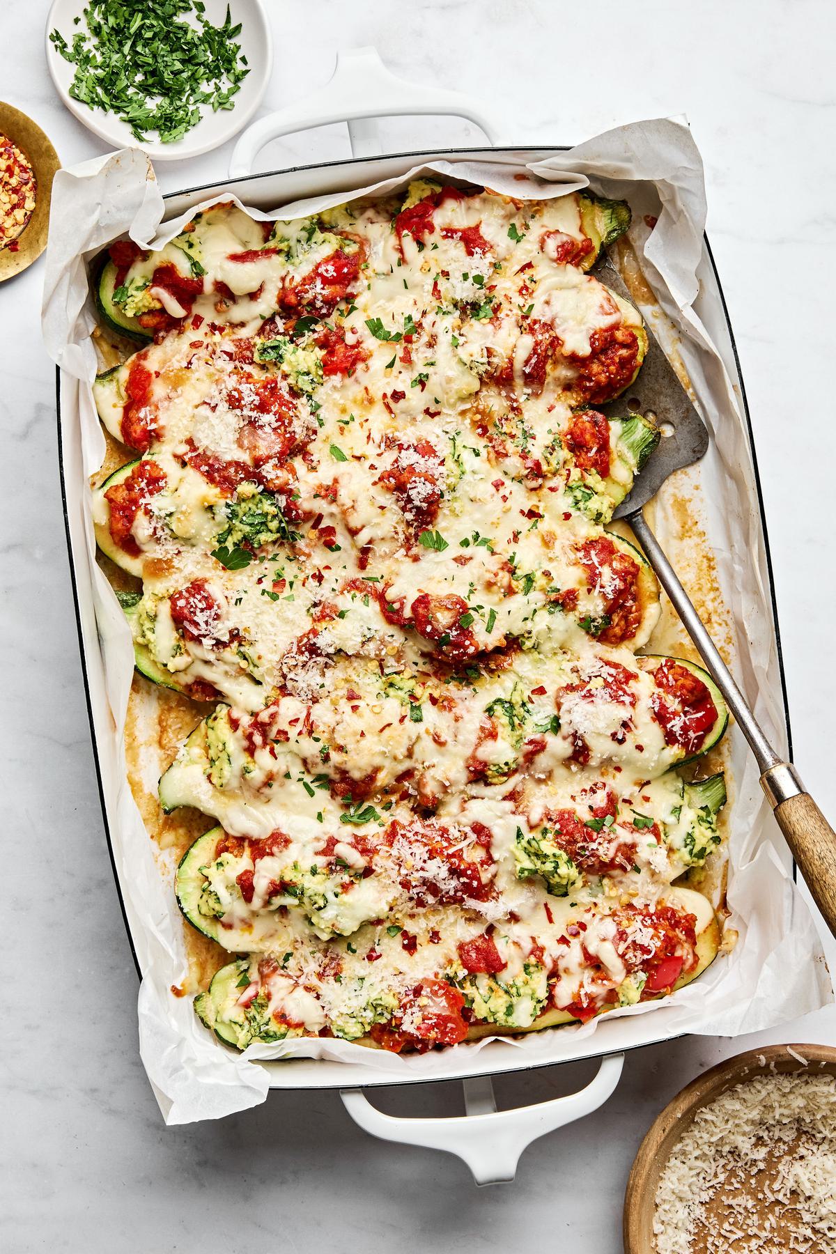 lasagna stuffed zucchini boats in a baking dish sprinkled with Parmesan, parsley and red pepper flakes