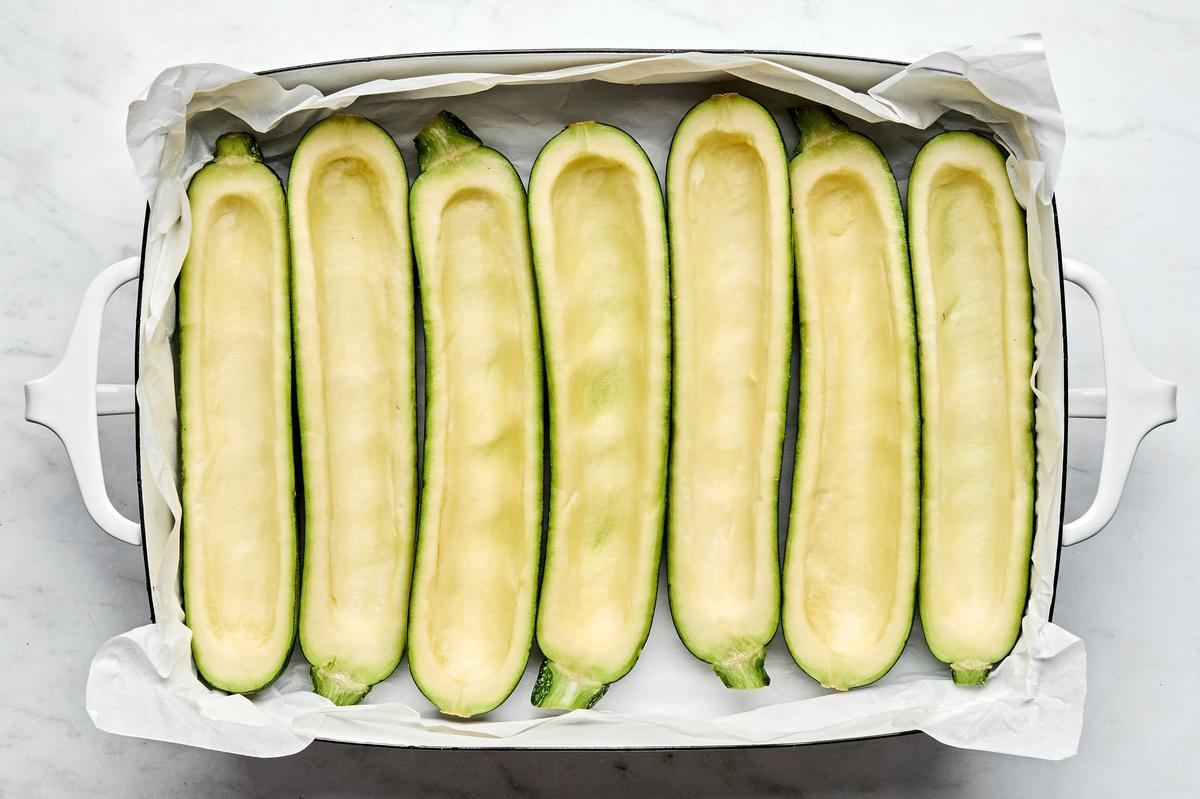 4 zucchinis sliced in half with the inside scooped out in a parchment lined baking dish