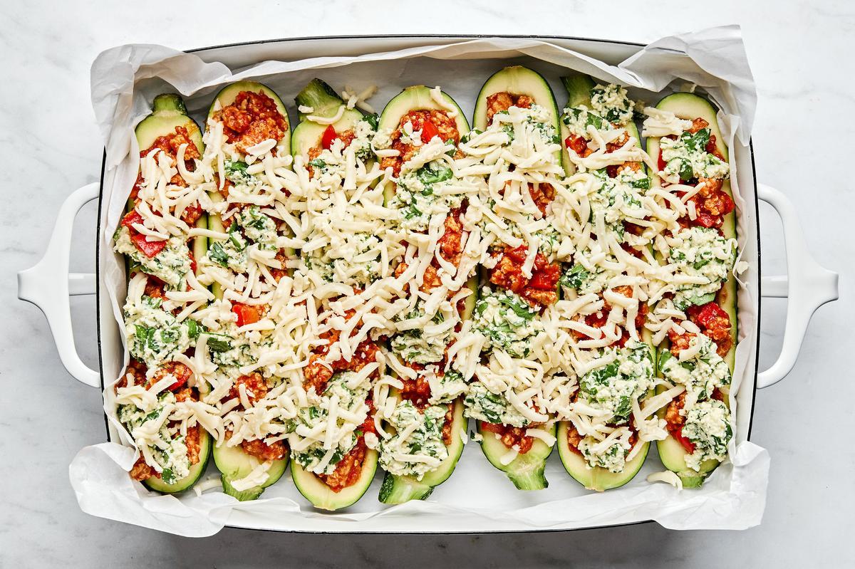 lasagna stuffed zucchini goats in a parchment lined baking dish sprinkled with mozzarella cheese