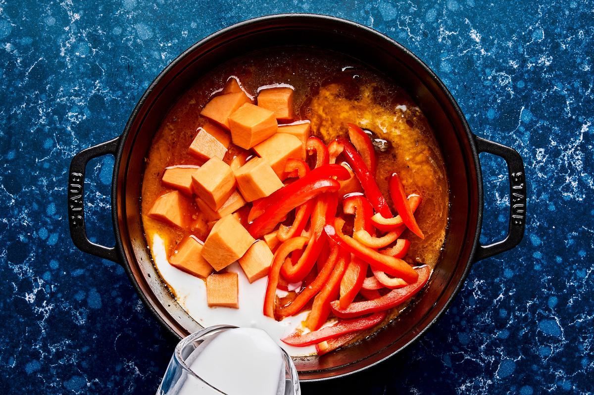 coconut milk, sweet potatoes and bell peppers cooking in a red curry sauce in a pot