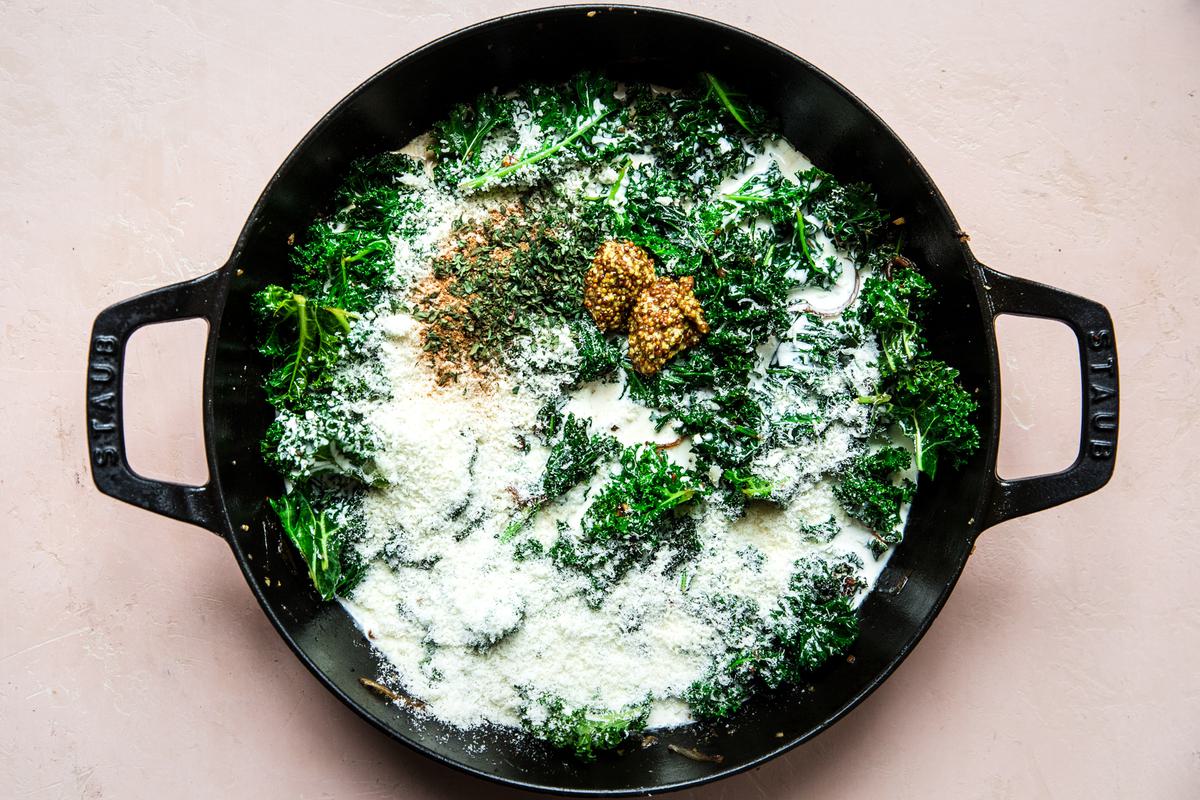 shallots, garlic, kale heavy cream, Parmesan, mustard, thyme, nutmeg and salt being cooked in a skillet