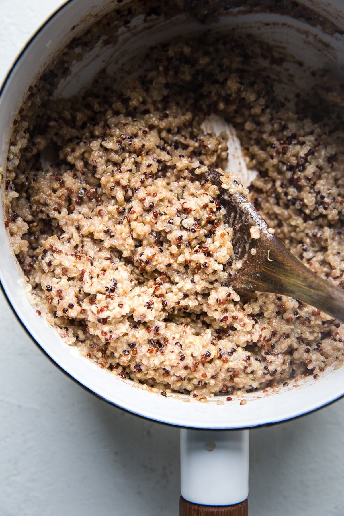 quinoa breakfast with coconut milk in a small pot with a wooden spoon