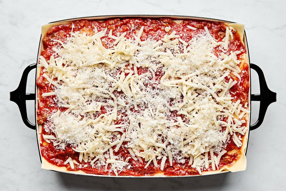 meat sauce, lasagna noodles and ricotta mixture being layered in a baking dish topped with mozzarella and Parmesan