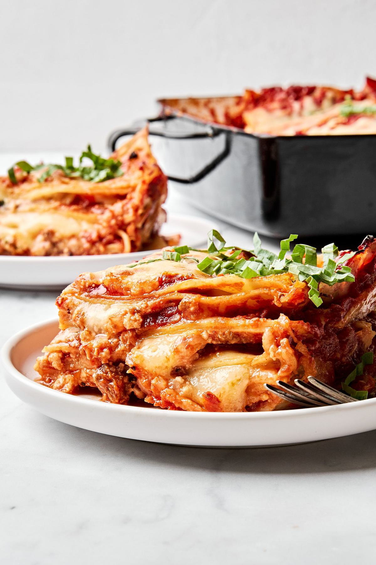 a pan of classic lasagna made with meat sauce, mozzarella, Parm, ricotta, and lasagna noodles being dished on to plates