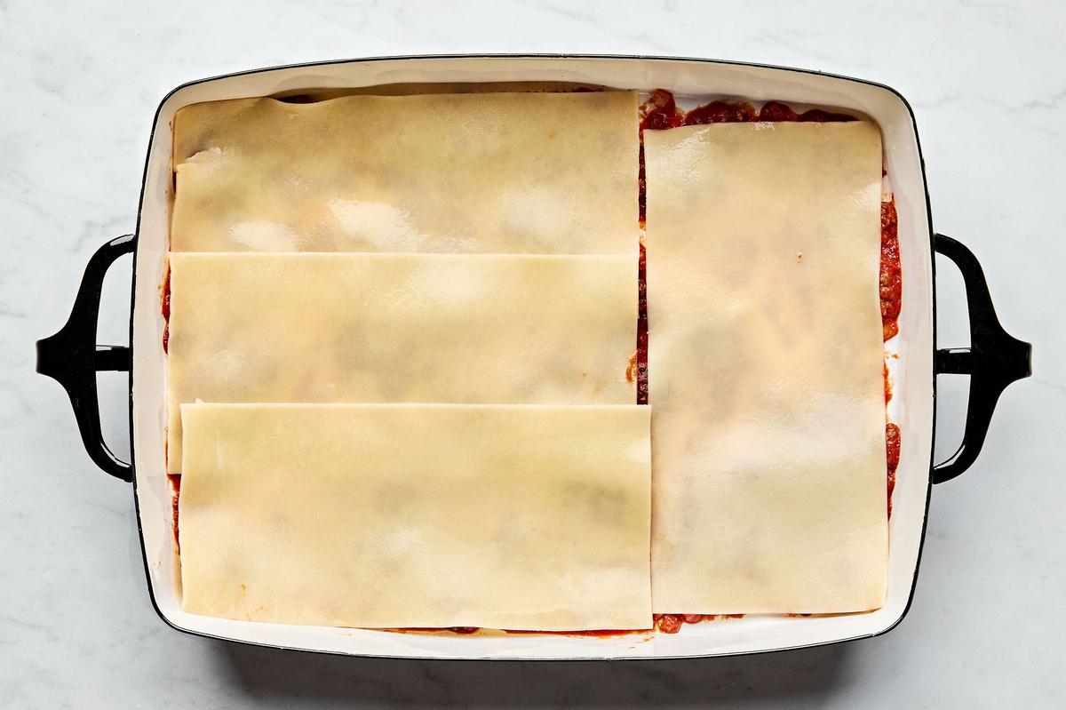 meat sauce, lasagna noodles and ricotta mixture being layered in a baking dish