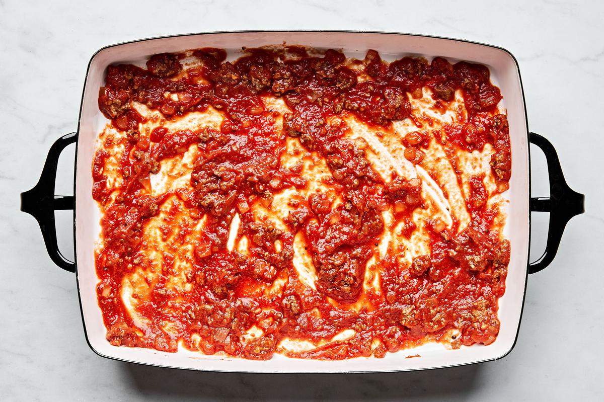 meat sauce, lasagna noodles and ricotta mixture being layered in a baking dish