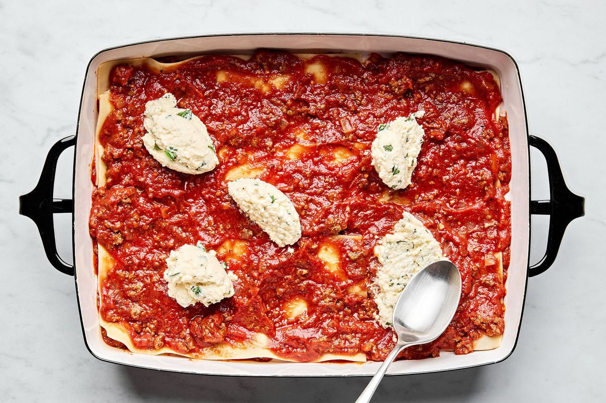 meat sauce, lasagna noodles and ricotta mixture being layered in a baking dish