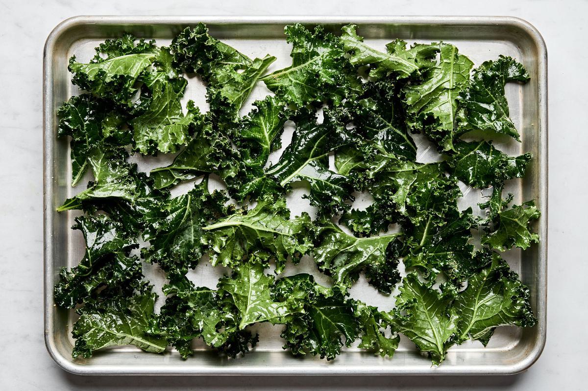 Raw kale leaves, tossed in oil and seasoning, arranged on a baking sheet, ready to be baked into crispy kale chips.
