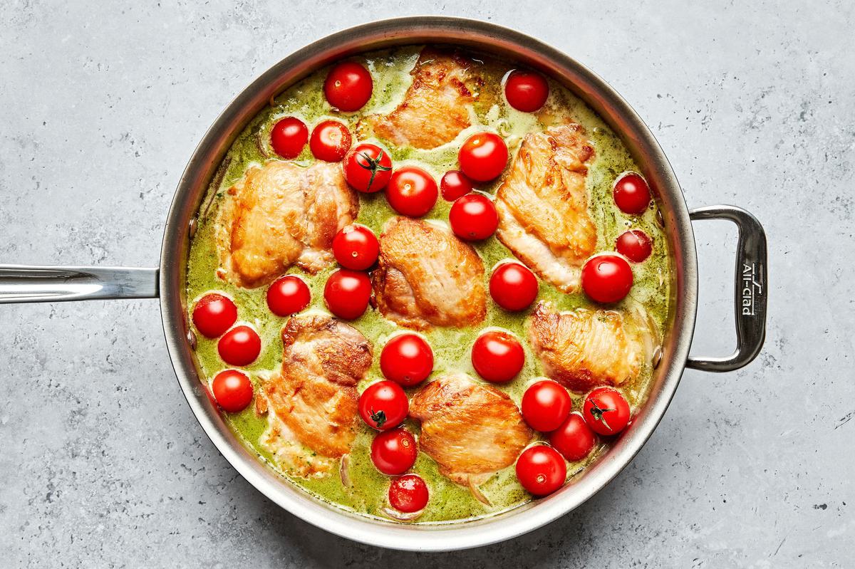 chicken thighs, cherry tomatoes, red onion, chicken stock, rice, pesto, lemon zest, lemon juice and salt cooking in a skillet